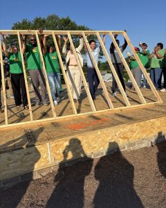 Organizational leaders participate in a ceremonial wall raising by lifting a wooden frame together